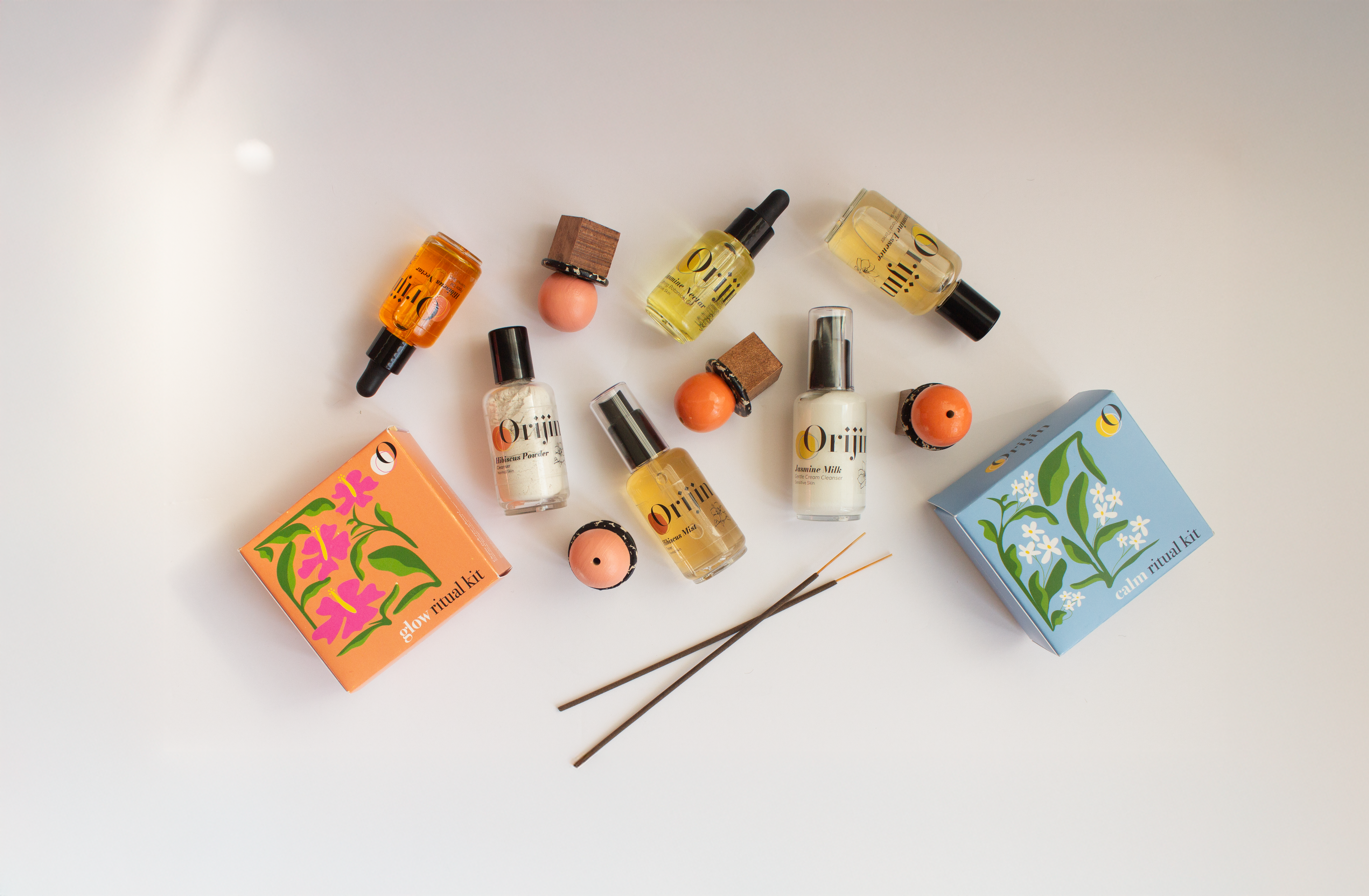 Collection of Oriji skincare products including bottles, gift boxes, and incense sticks on a light background